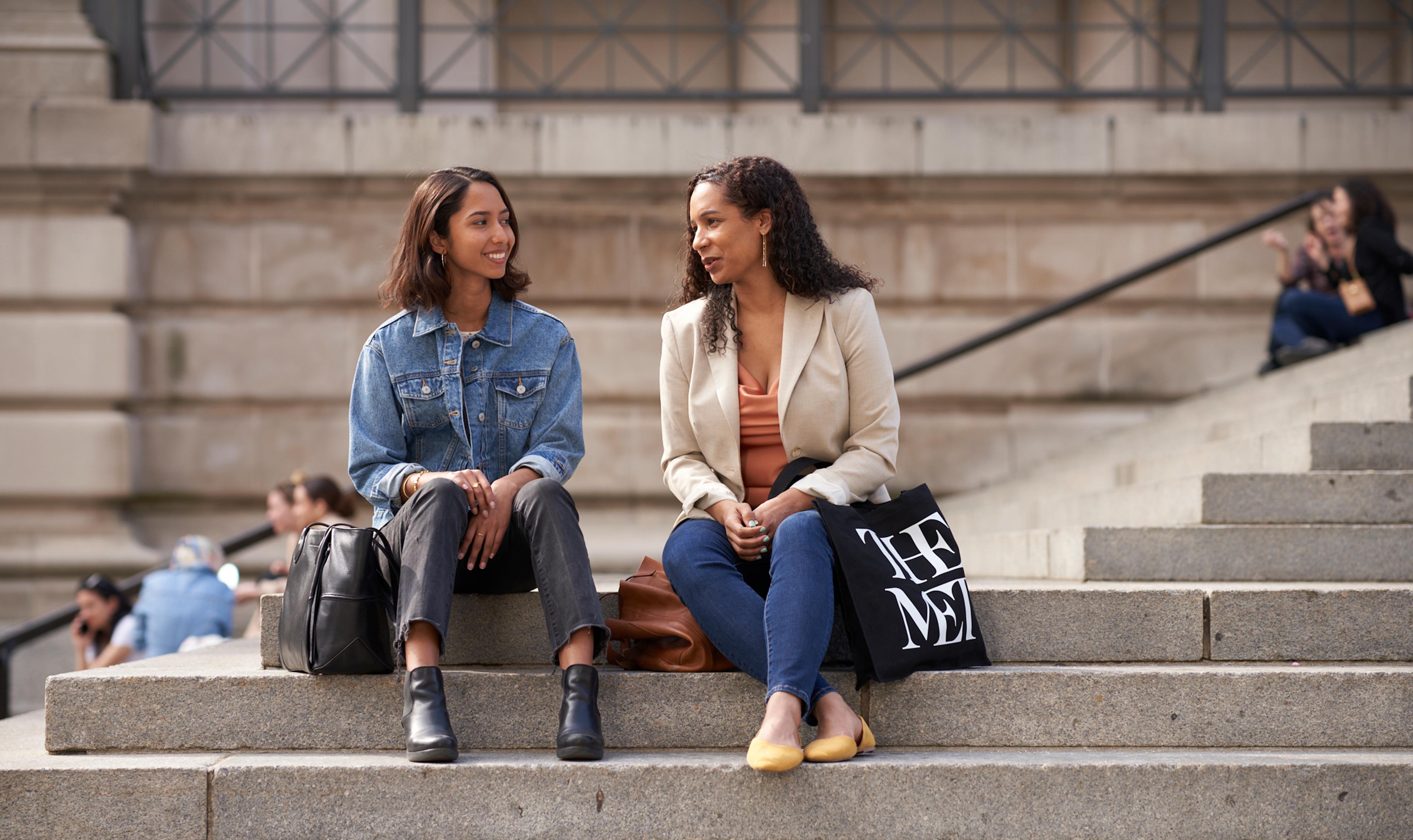 Two women sit chatting on The Met steps.